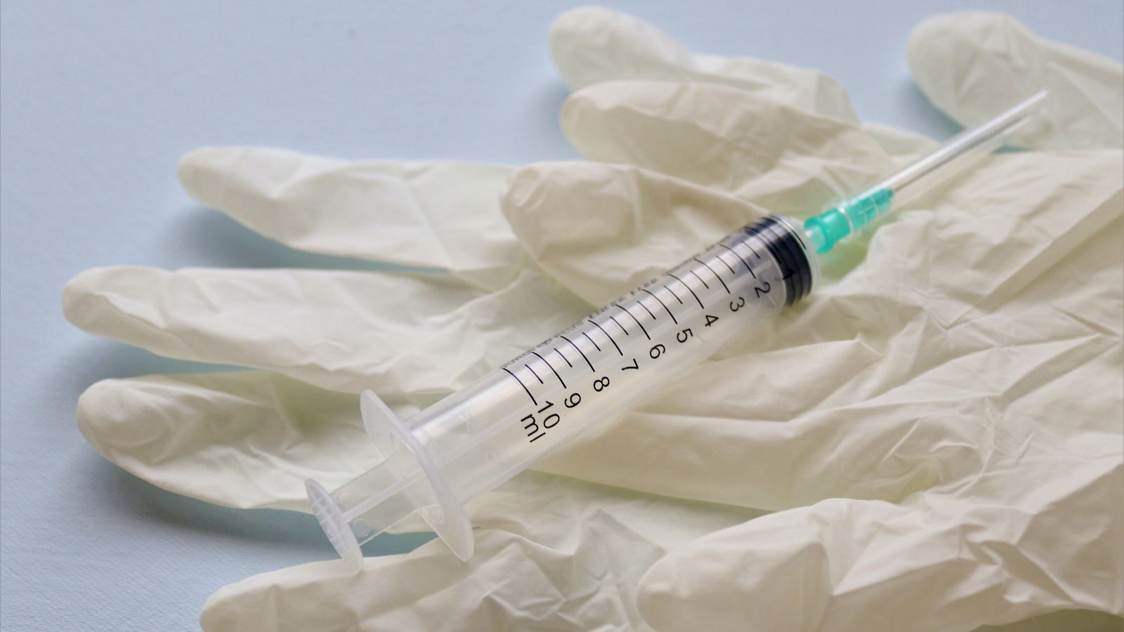 Close-up of a syringe resting beside medical gloves on a flat surface.