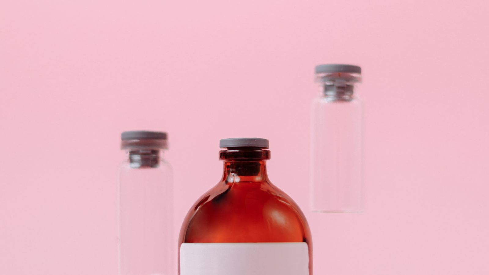 Studio shot of sterile brown and clear glass vials arranged against a pink background.