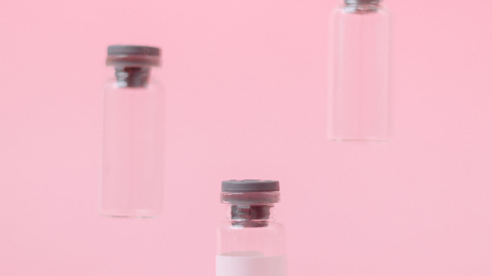 Three empty medical vials floating against a soft pink background.